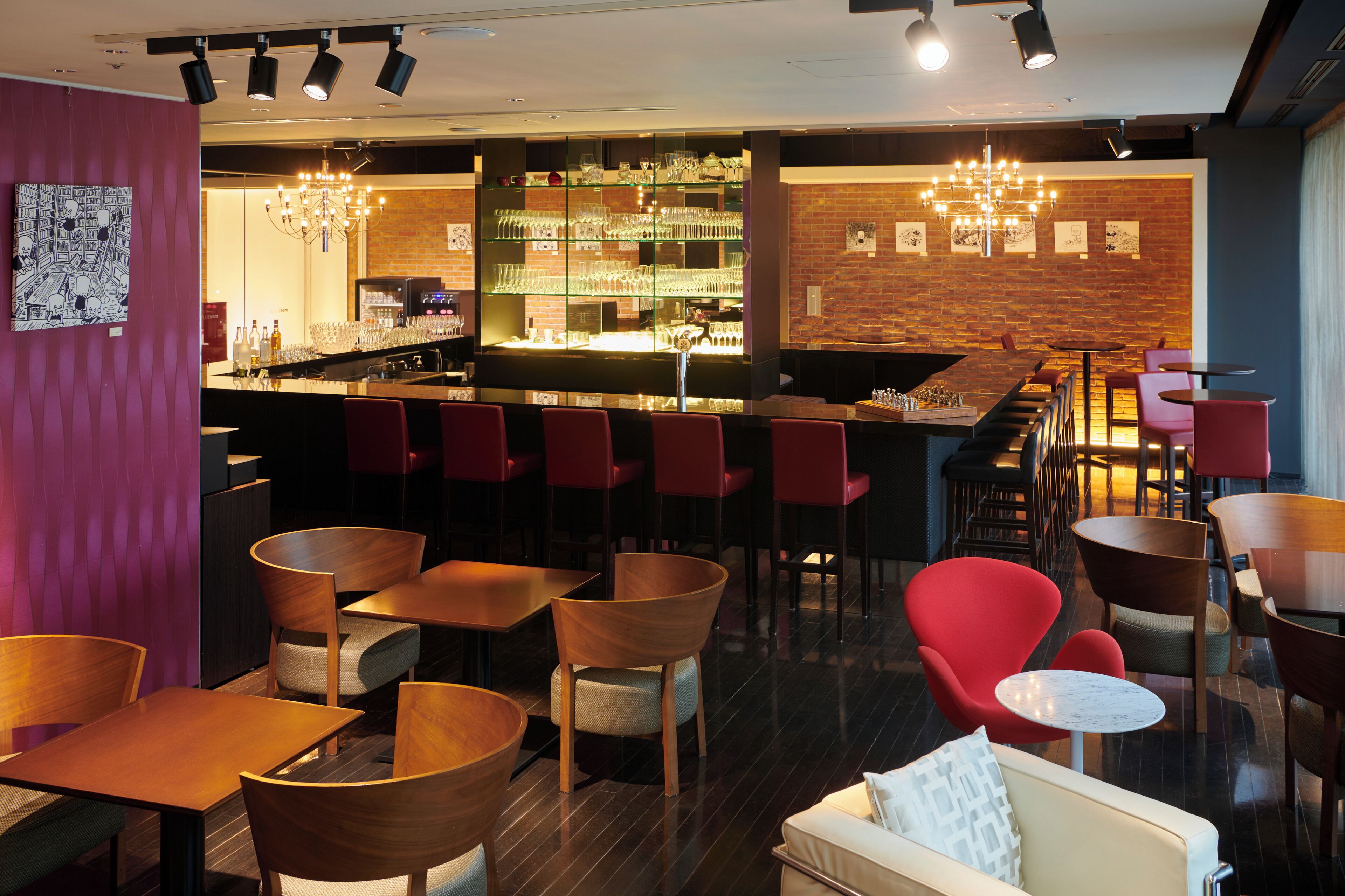 Zona de bar con pared de ladrillo, sillas rojas y barra con vasos y botellas.