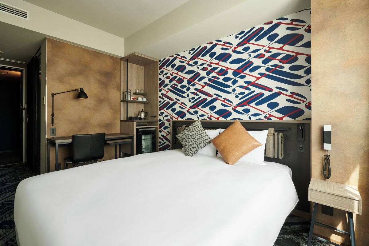 A hotel room with a large bed, a desk, and a minibar.