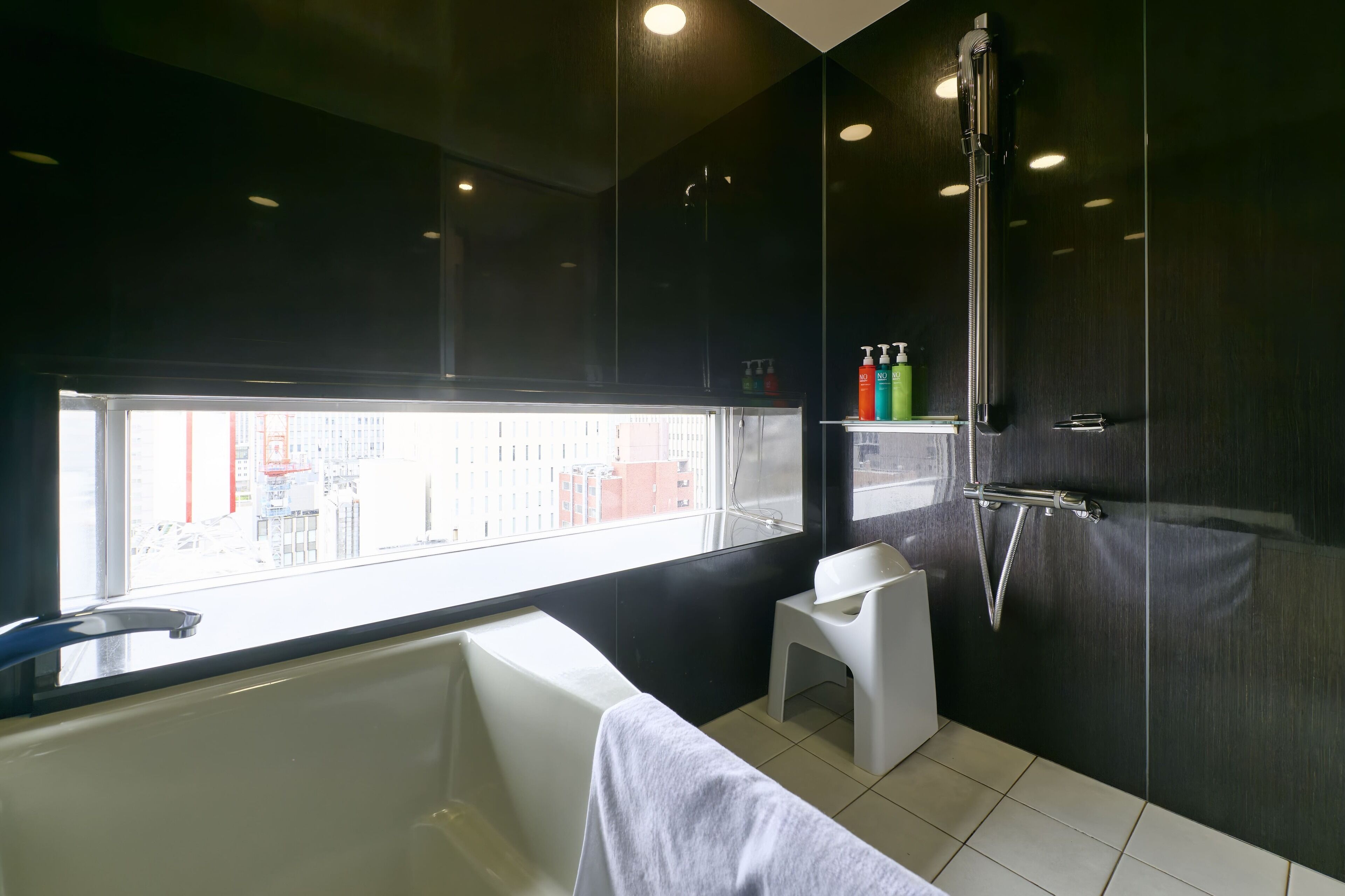 Ein modernes Badezimmer mit Badewanne, einer kleinen Sitzgelegenheit, einer Dusche und einem Fenster mit Blick auf die Stadt.