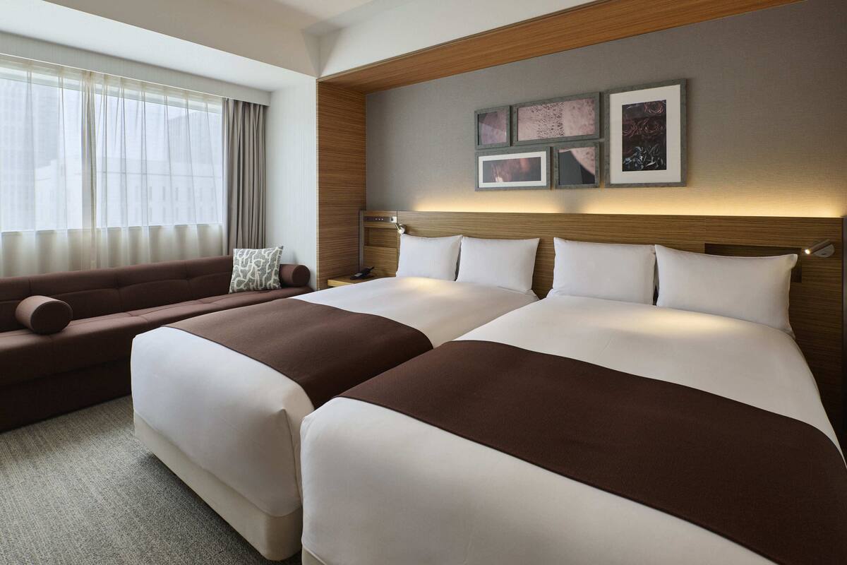 A hotel room with two beds, a sofa, and a large window with curtains.