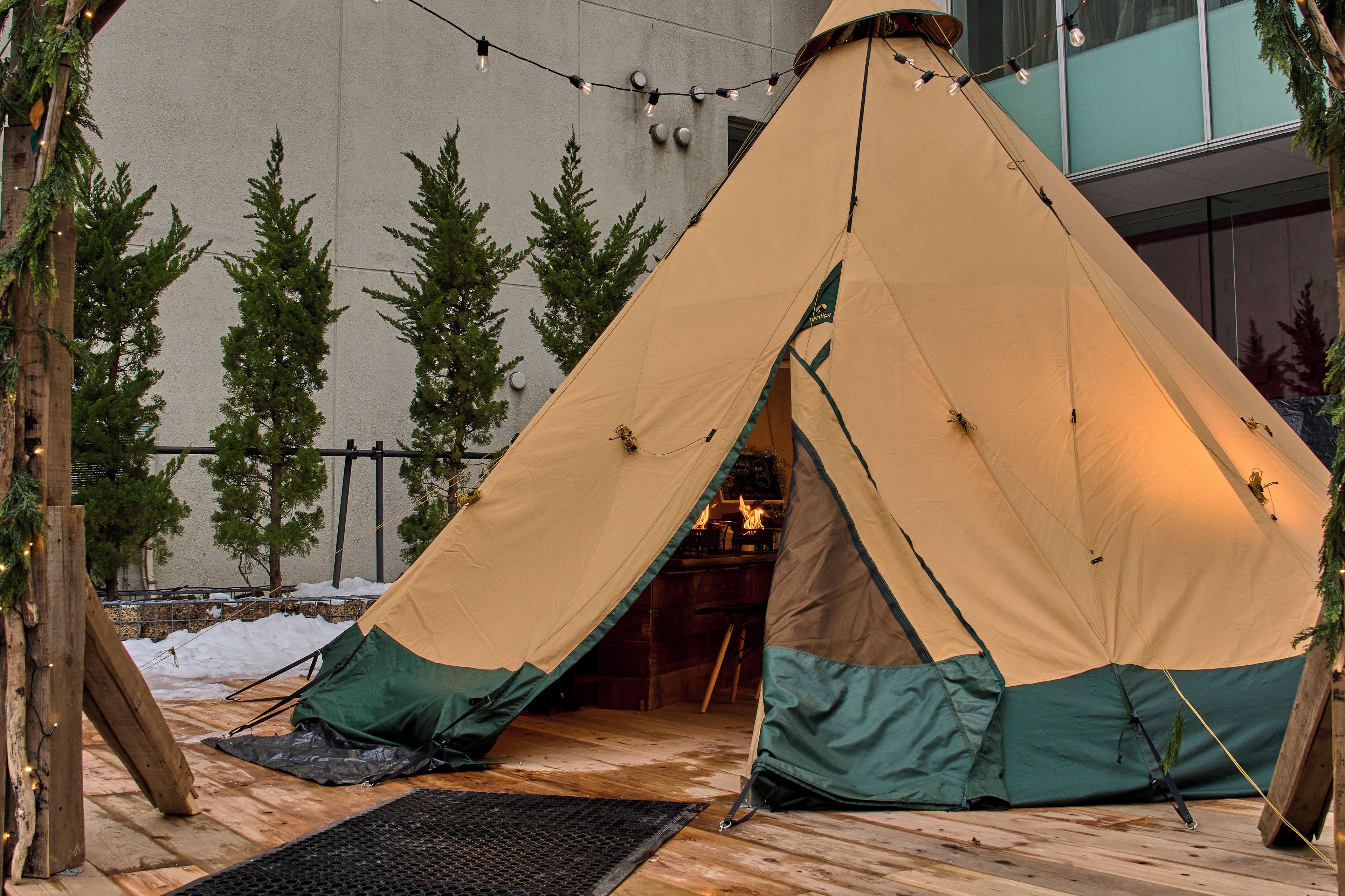 Una carpa montada sobre una terraza de madera, con vista a un edificio y árboles al fondo.