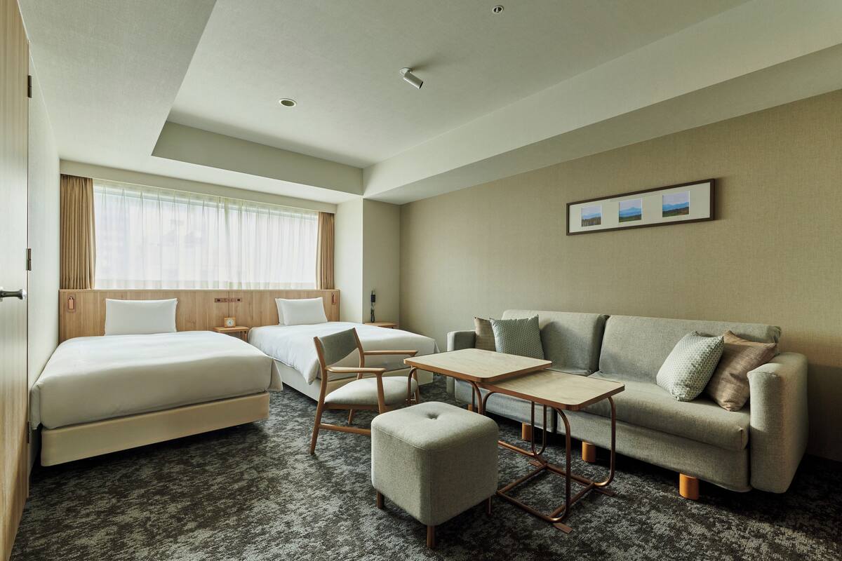 A hotel room with a bed, two sofas, a small table, and a window with curtains.