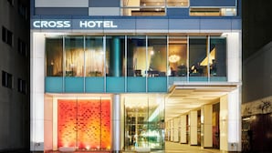 Un hotel moderno con fachada de vidrio, una entrada destacada y un área de estar visible al aire libre.