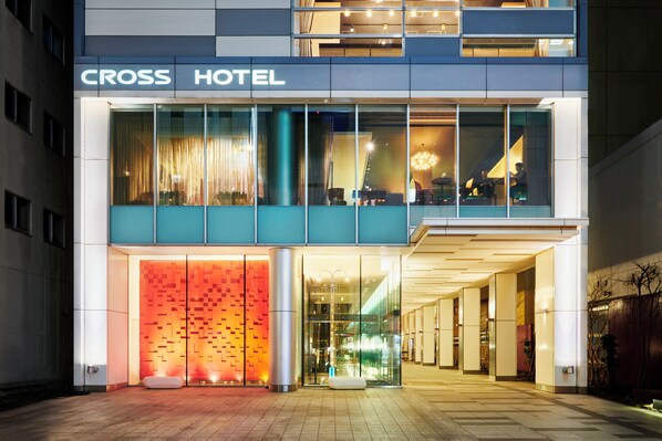 A modern hotel with a glass facade, a prominent entrance, and a visible seating area outside.