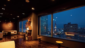 Una habitación de hotel moderna con un amplio ventanal que ofrece vista a la ciudad, suelo de madera y muebles contemporáneos.