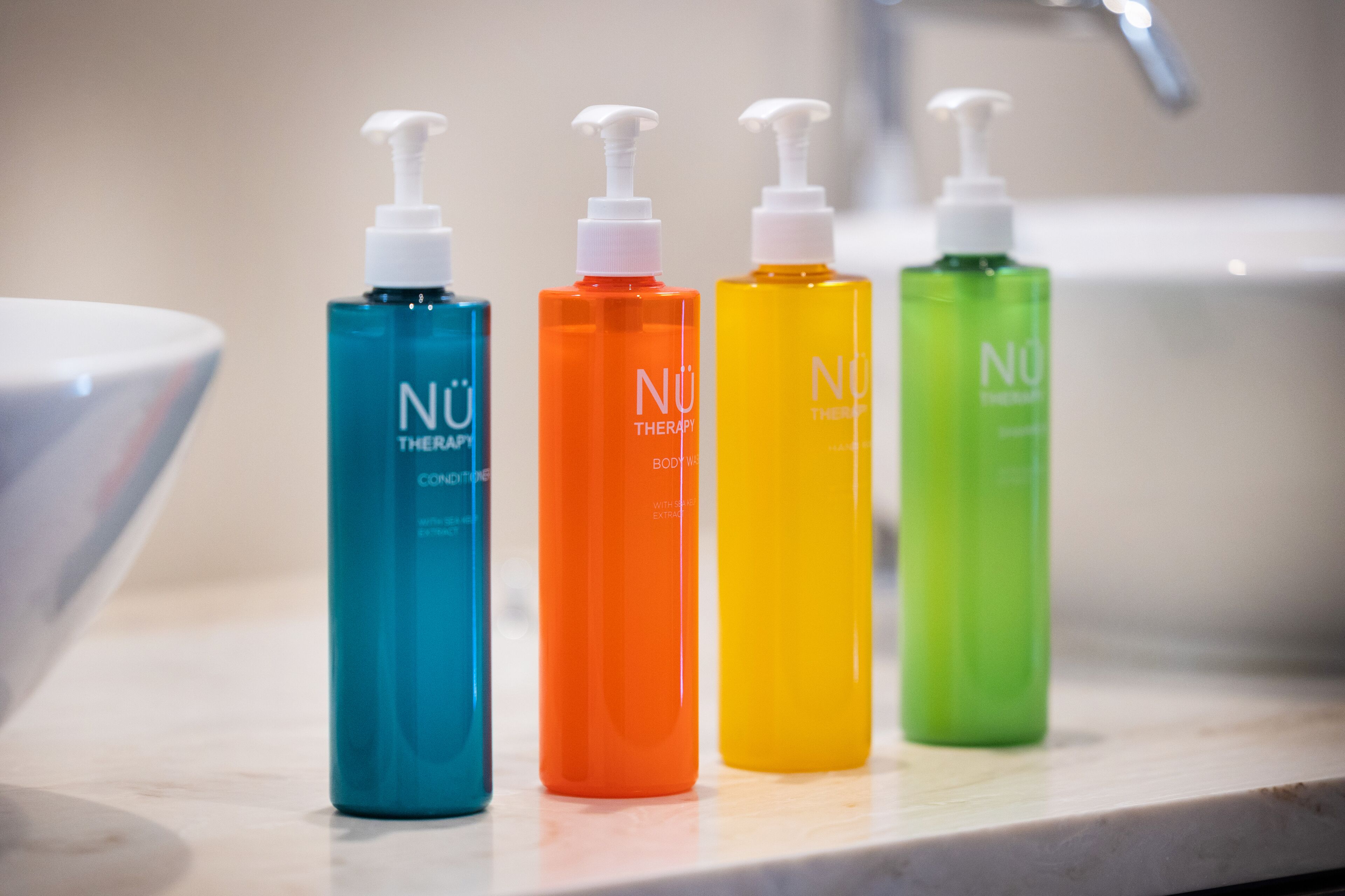 Quatre bouteilles de gel douche Nü Therapy sur le comptoir d’une salle de bain.