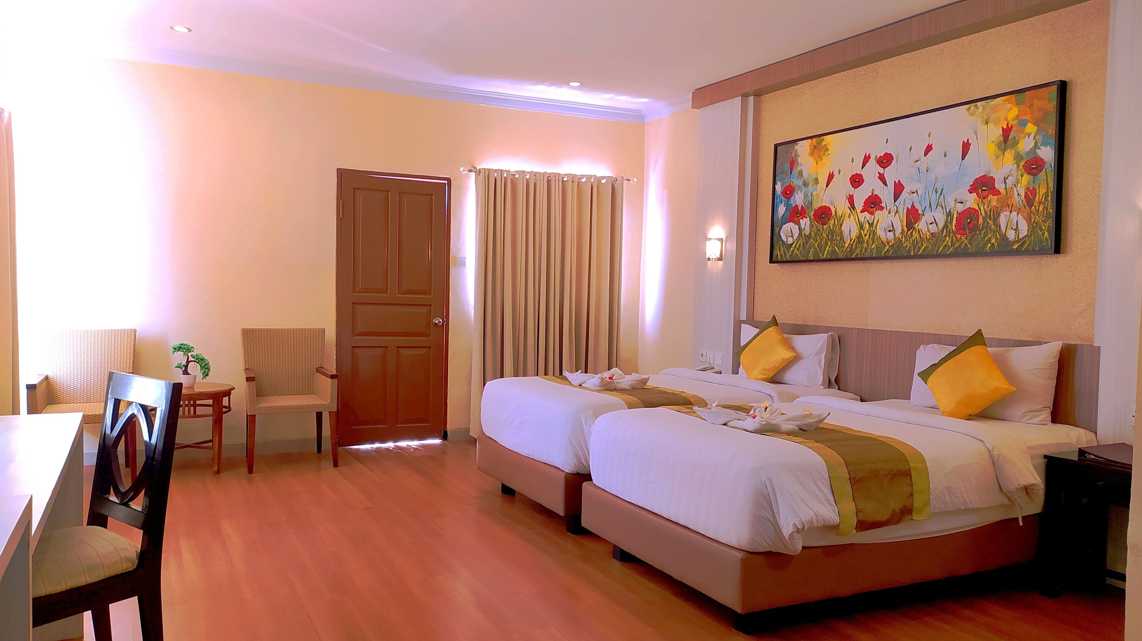 A hotel room with two beds, a dining area, a chair, a door, and a painting on the wall.