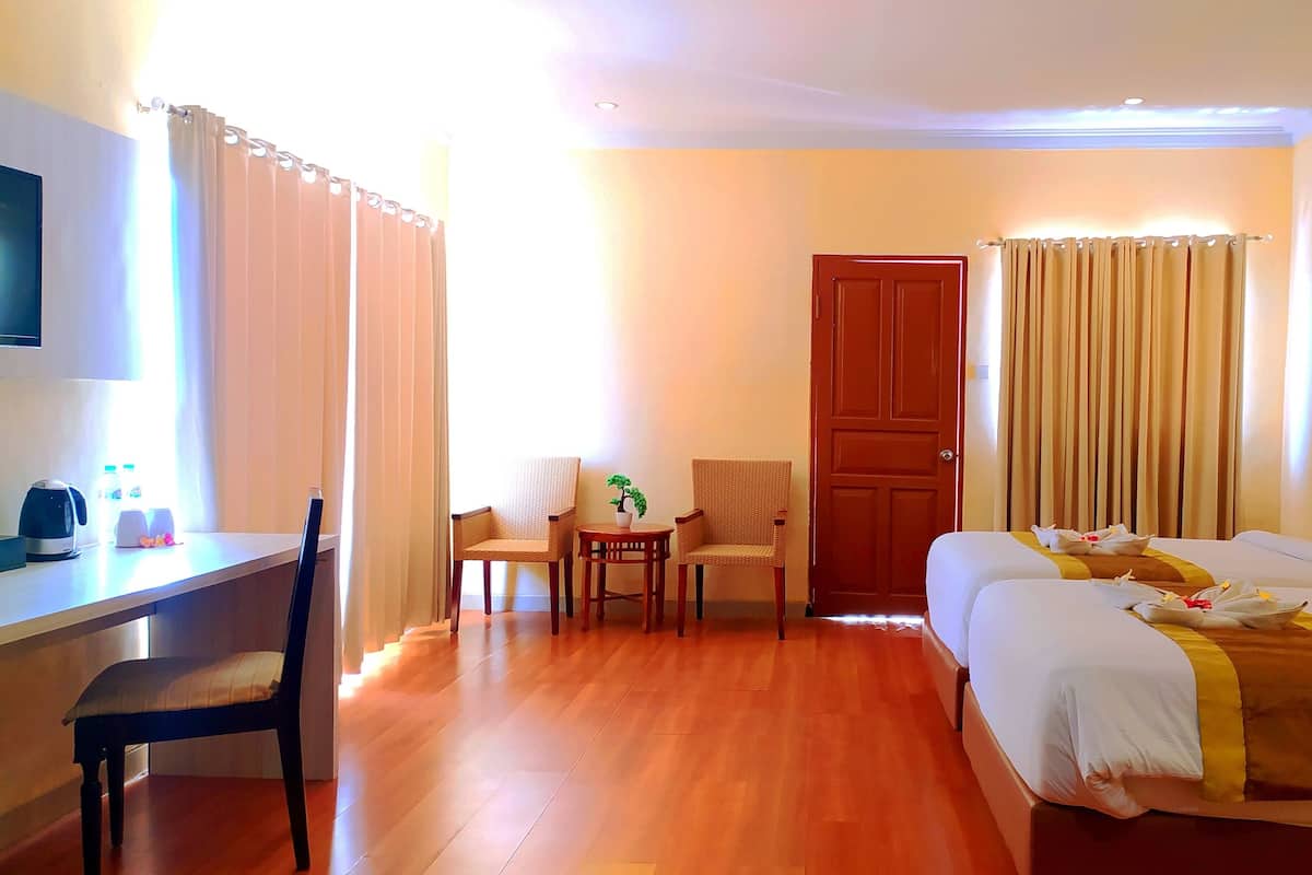A hotel room with a wooden floor, a desk with a chair, two beds with towels, a door, and a painting on the wall.