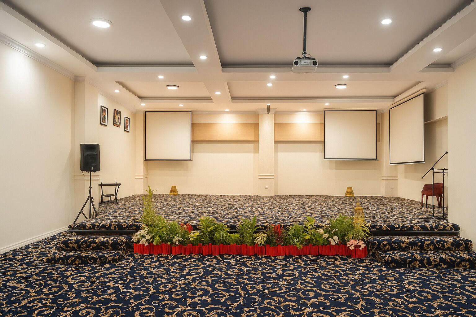 Un salón de conferencias con alfombra estampada, un escenario con atril y un proyector en el techo.