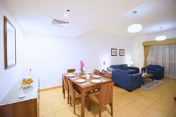 A modern living room with a dining area, blue sofas, and a wooden dining table.