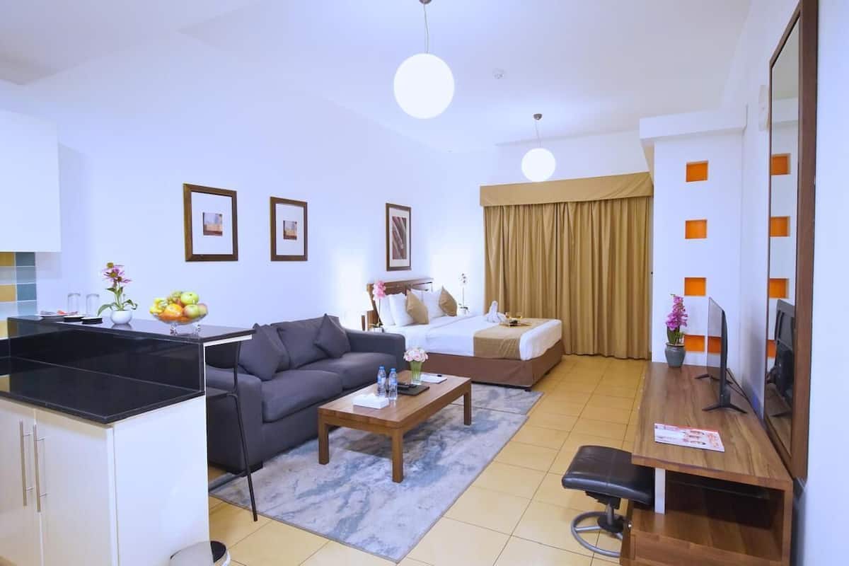 A hotel room with a kitchenette, a sofa, a bed, a desk, and a television.