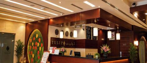 A hotel reception area with a wooden reception desk, a large tulip-themed artwork, a clock, and a reception sign.
