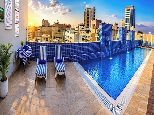 A rooftop pool with lounge chairs, a cityscape view, and a tiled pool edge.