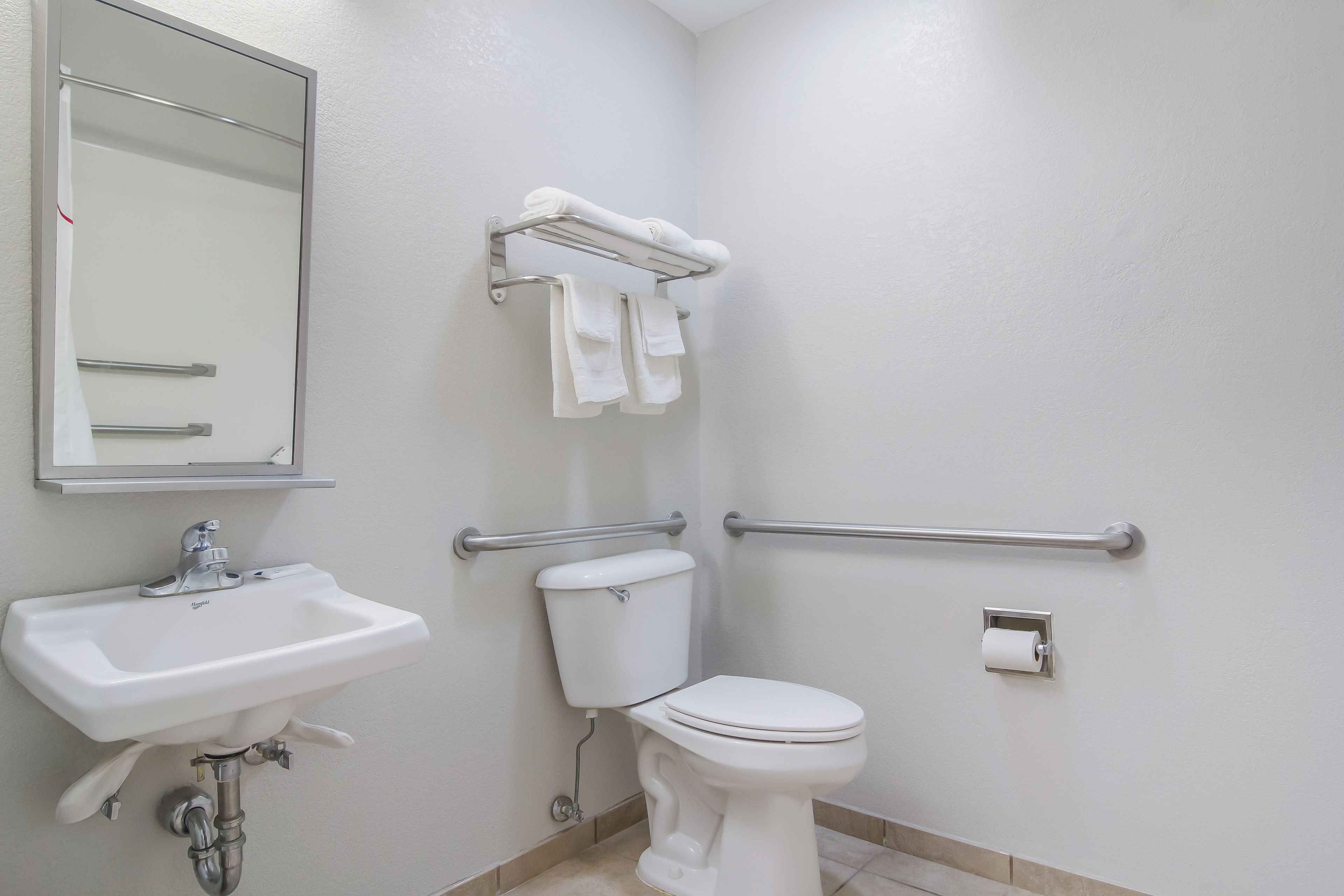 A bathroom with a sink, toilet, and handrails.