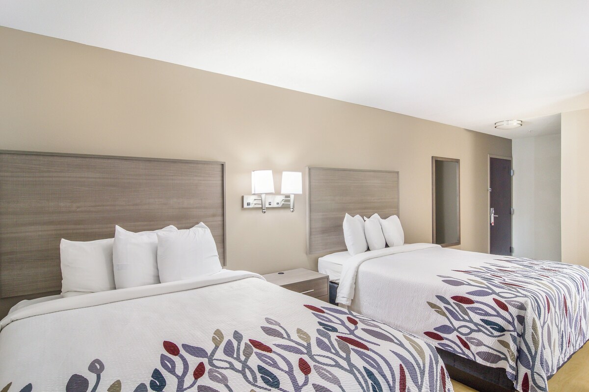 A hotel room with two beds, a nightstand, a wall-mounted lamp, and a door.
