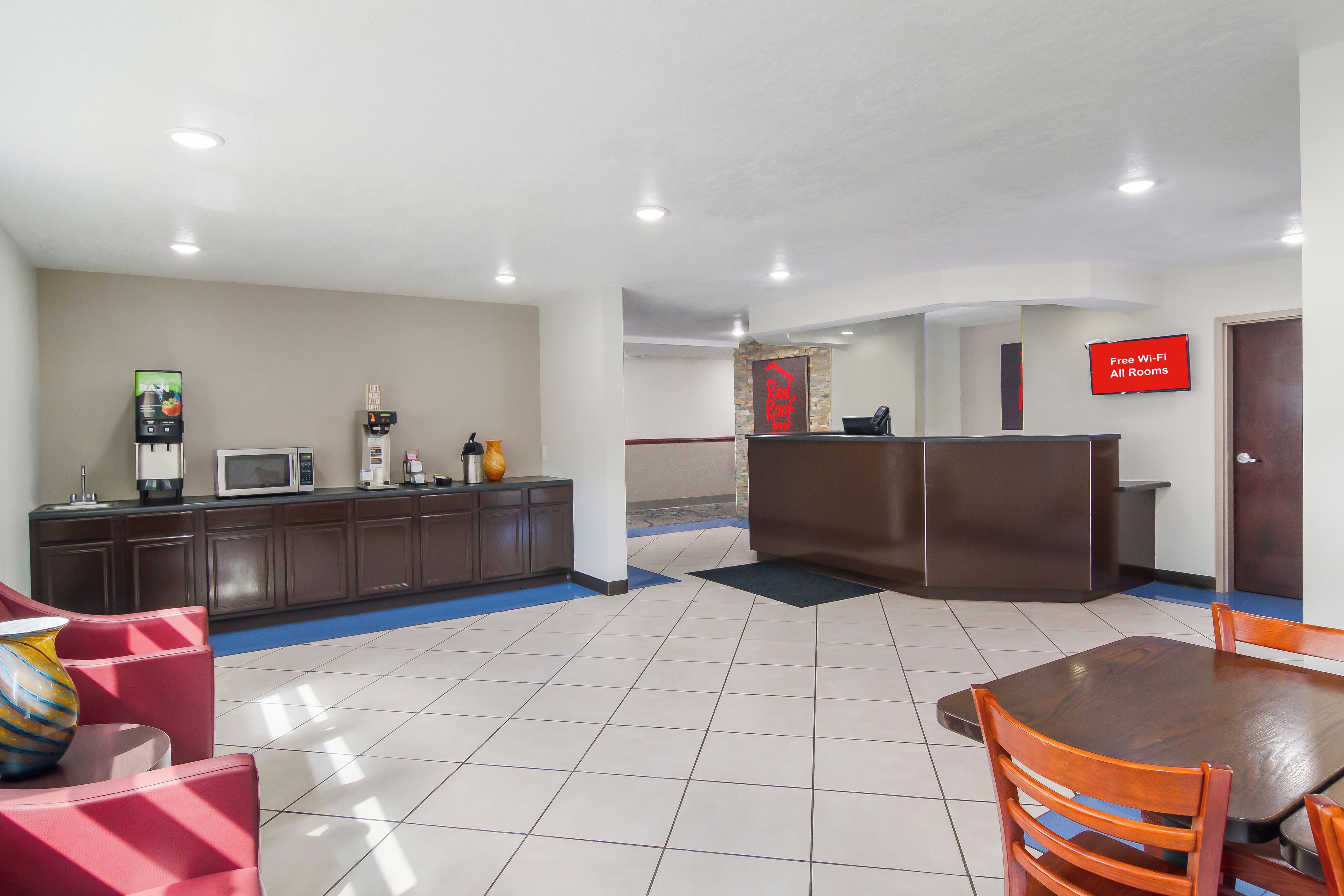 Un vestíbulo de hotel con mostrador de recepción, máquina de café, microondas y zona de estar con mesa y sillas.