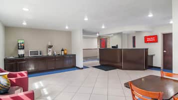 Un vestíbulo de hotel con mostrador de recepción, máquina de café, microondas y zona de estar con mesa y sillas.