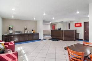 Un vestíbulo de hotel con mostrador de recepción, máquina de café, microondas y zona de estar con mesa y sillas.