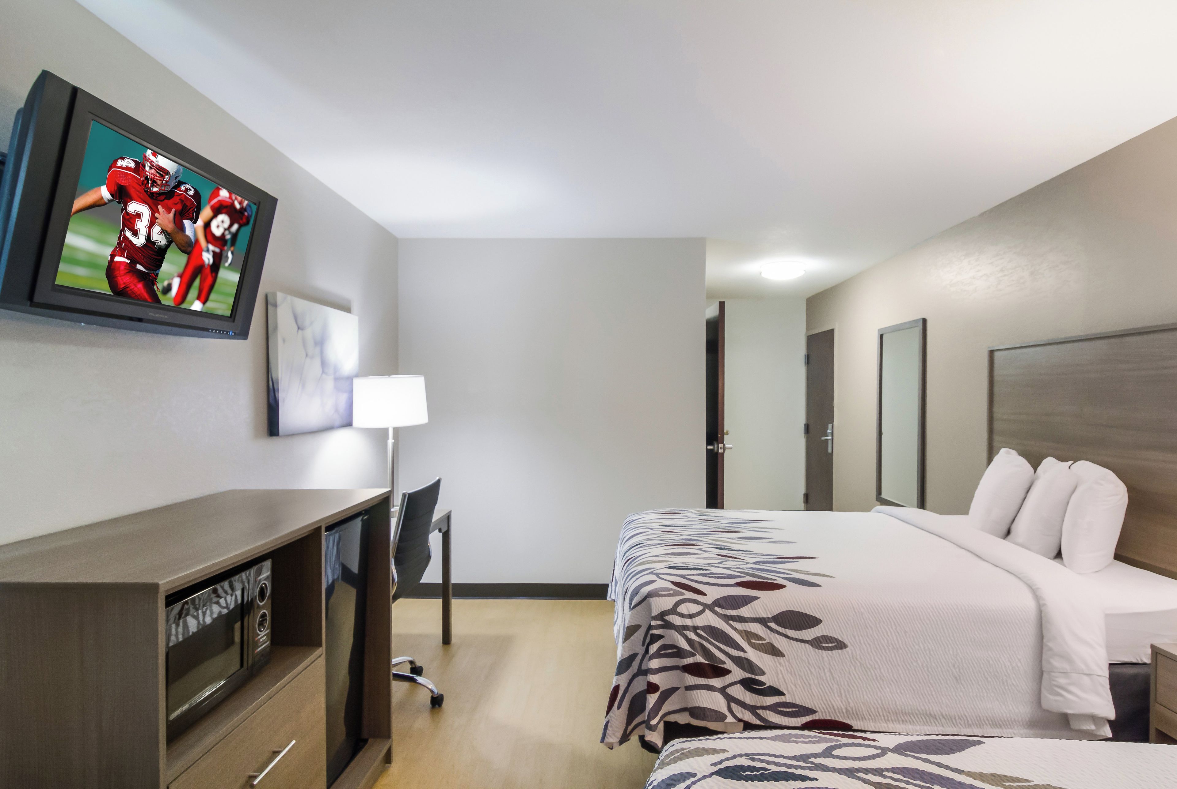 Une chambre d’hôtel avec un lit, un bureau, un téléviseur fixé au mur et une porte.