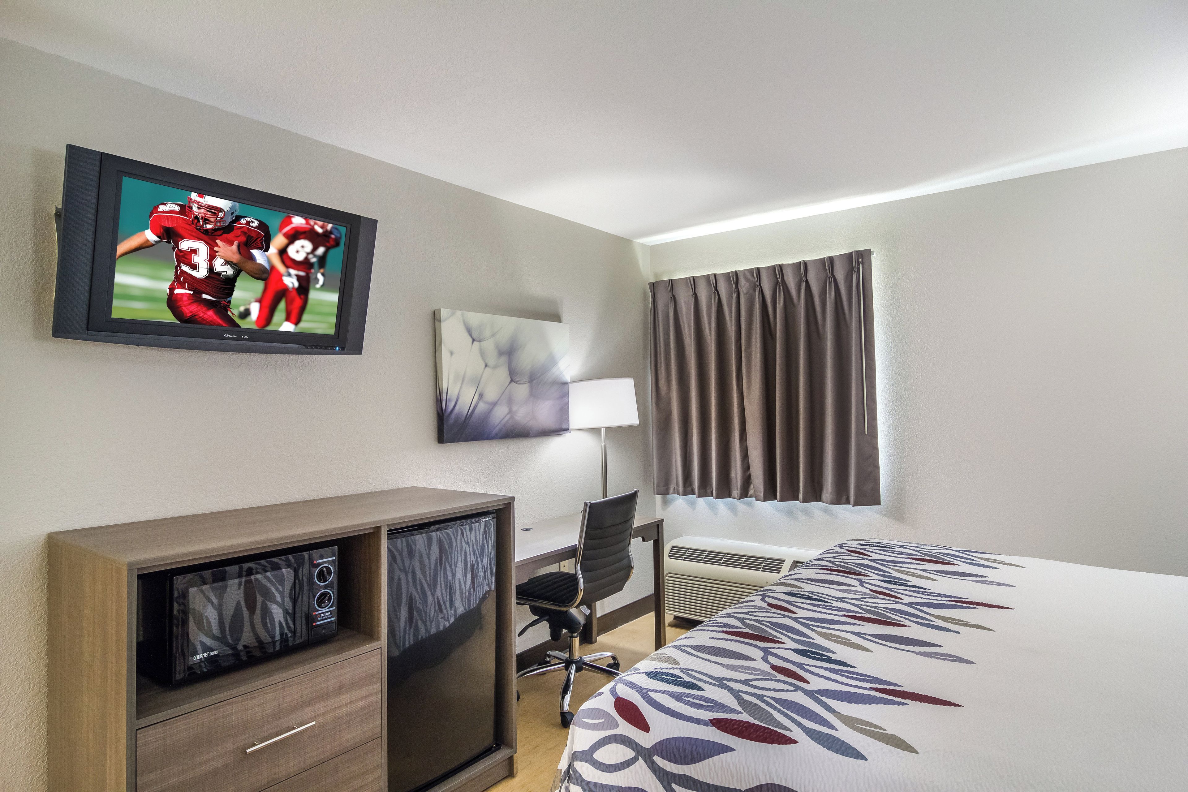 A hotel room with a bed, a desk, a television, a lamp, and a window with curtains.