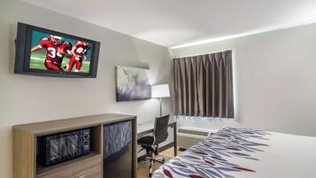 A hotel room with a bed, a desk, a television, a lamp, and a window with curtains.