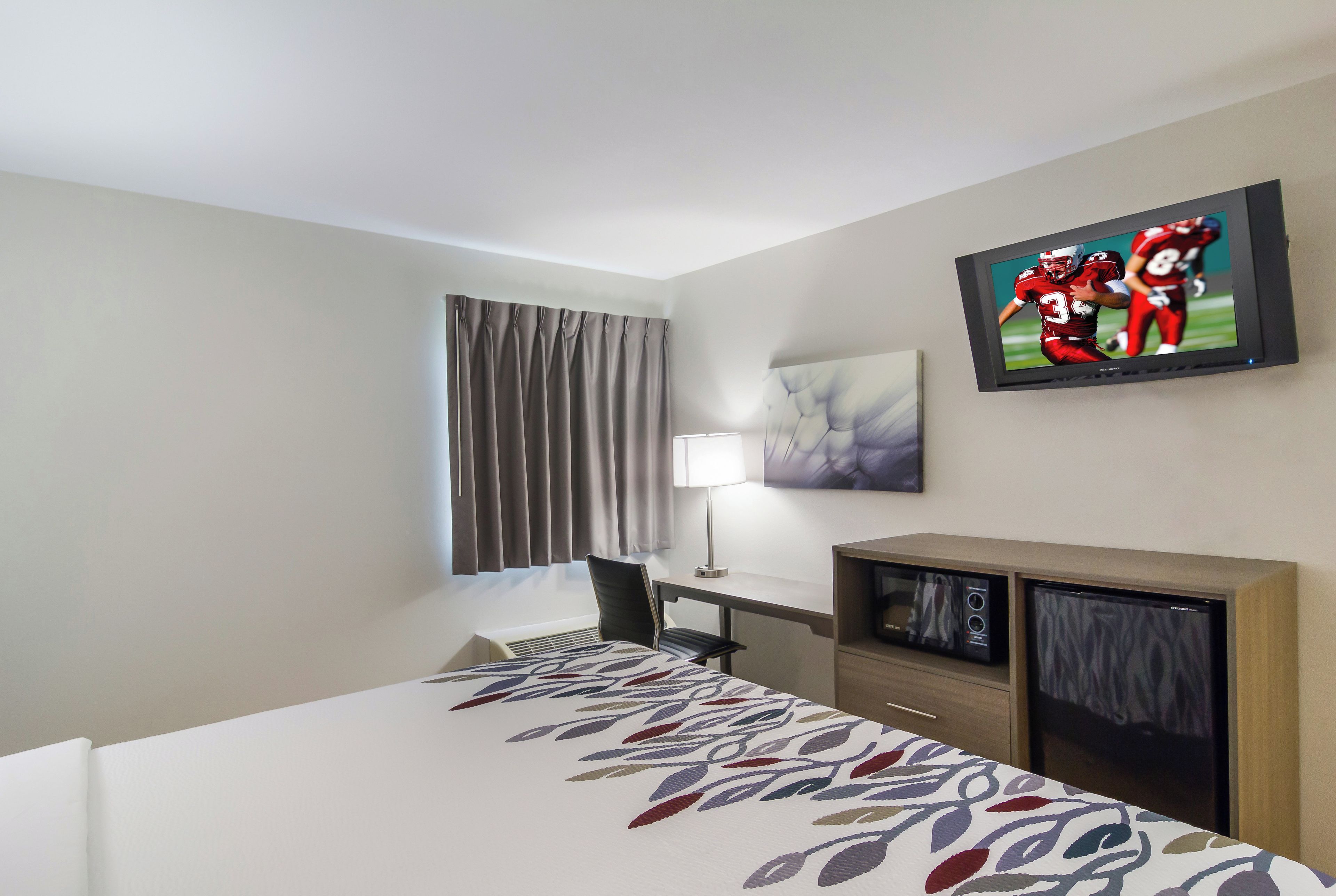 A hotel room with a bed, a desk, a chair, a television, and a window with curtains.