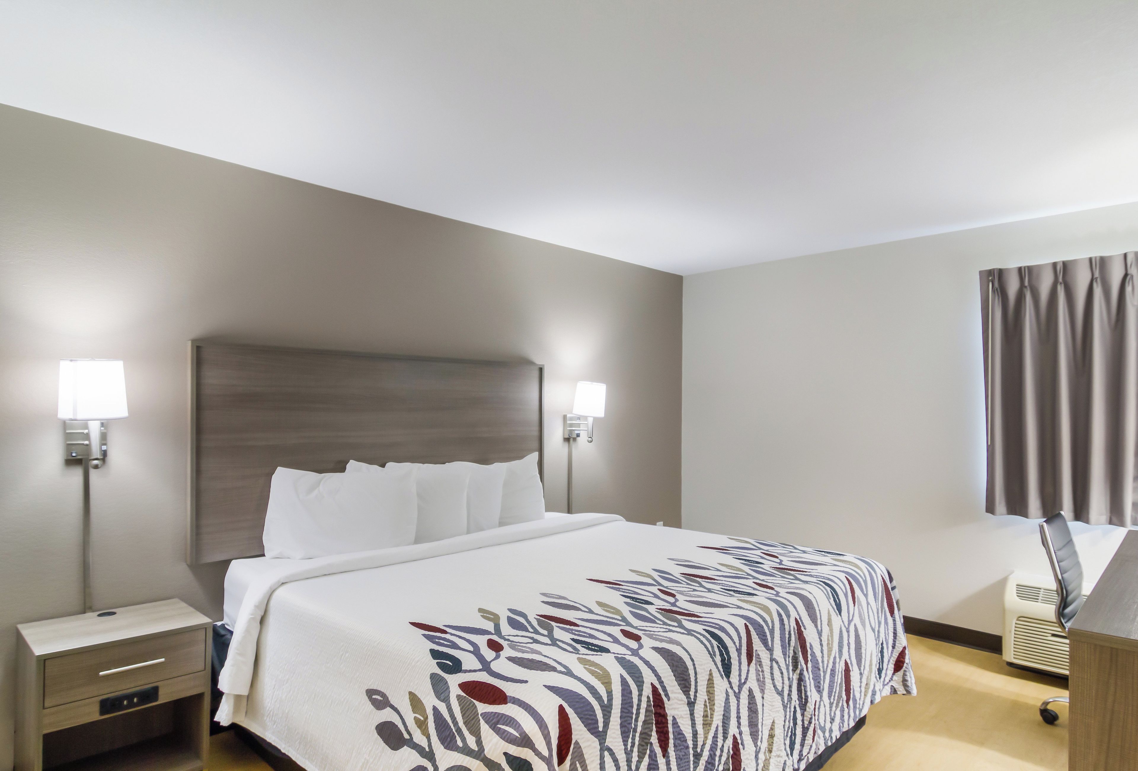 A hotel room with a bed, bedside tables, a desk, and a window with curtains.