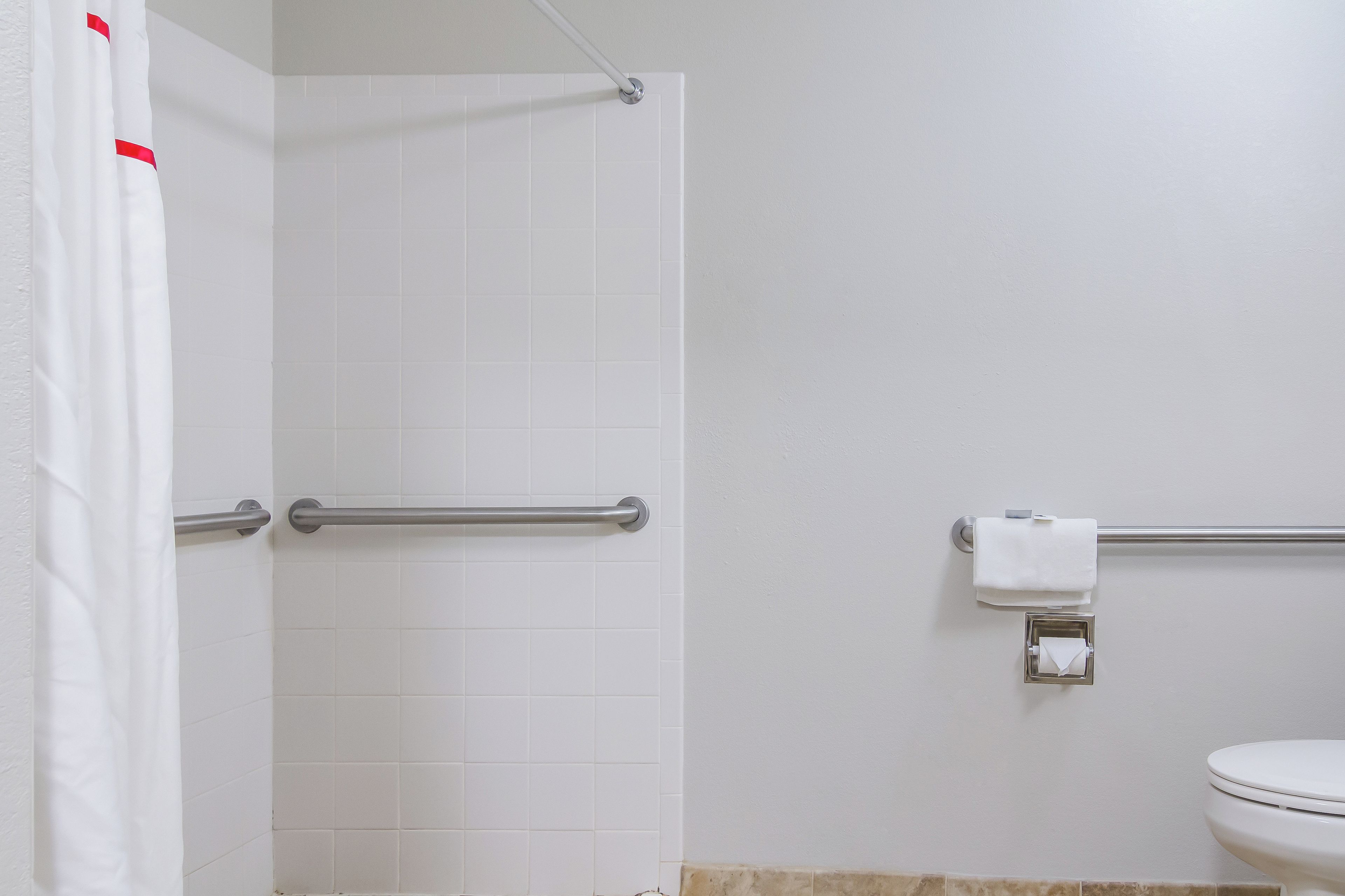 A bathroom with a shower curtain, grab bars, a toilet, and a towel dispenser.