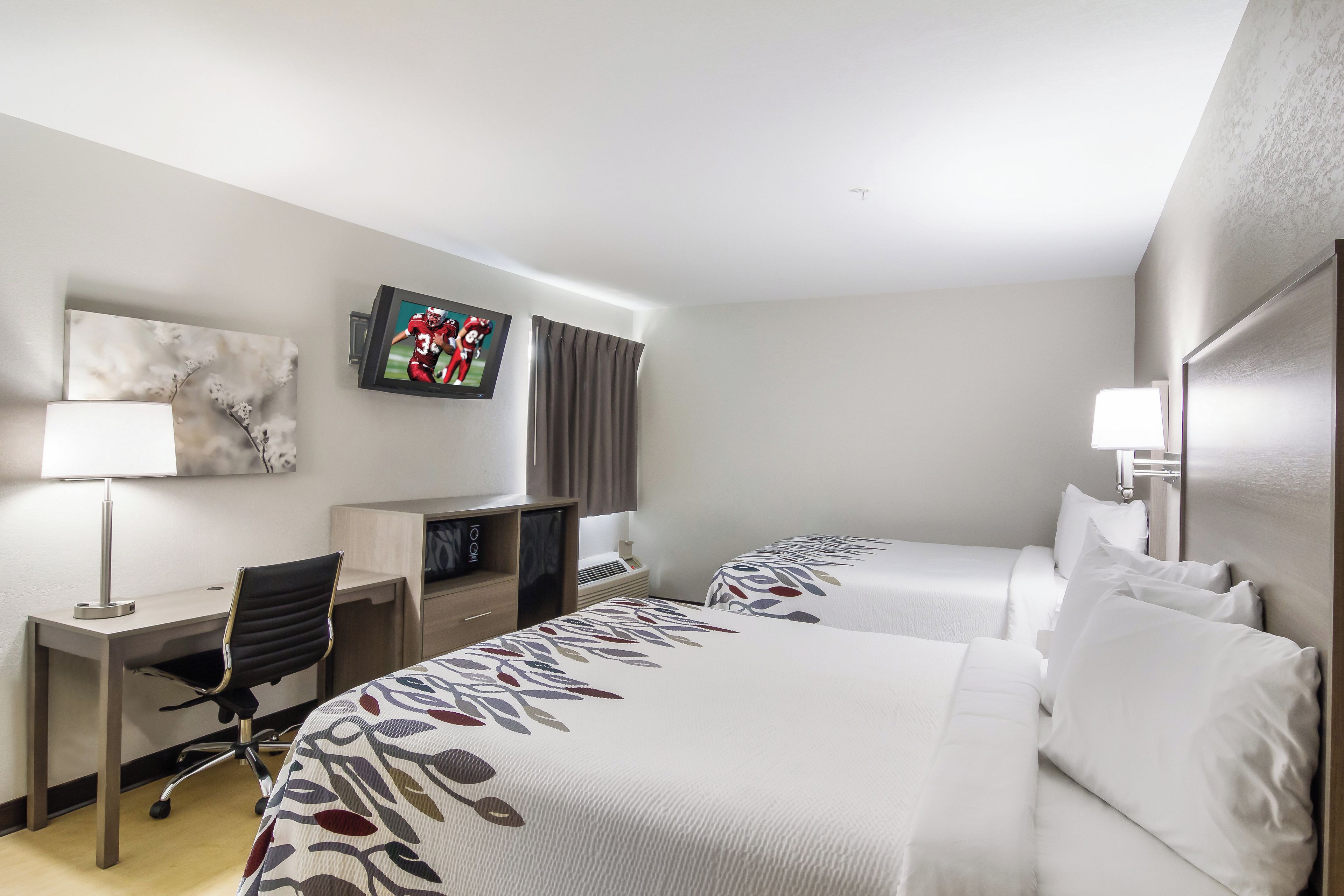 A hotel room with two beds, a desk, a chair, a TV, and a window with curtains.