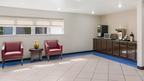 A waiting area with two red chairs, a small table with a vase, a microwave, and a coffee machine.