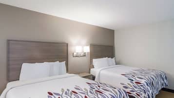 Quarto de hotel com duas camas, cada uma com cabeceira e mesa de cabeceira. Há duas luminárias fixadas na parede entre as camas.