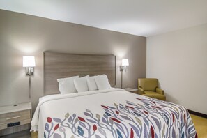 A hotel room with a bed, two bedside lamps, a chair, and a nightstand. - Red Roof Inn Darien - I-95/ North Brunswick (Darien)