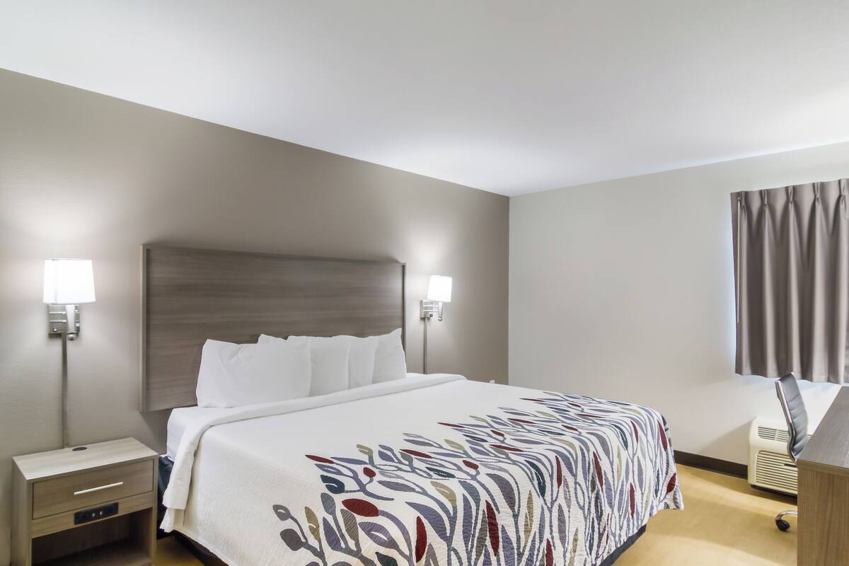 A hotel room with a bed, bedside lamps, a desk, and a window with curtains.