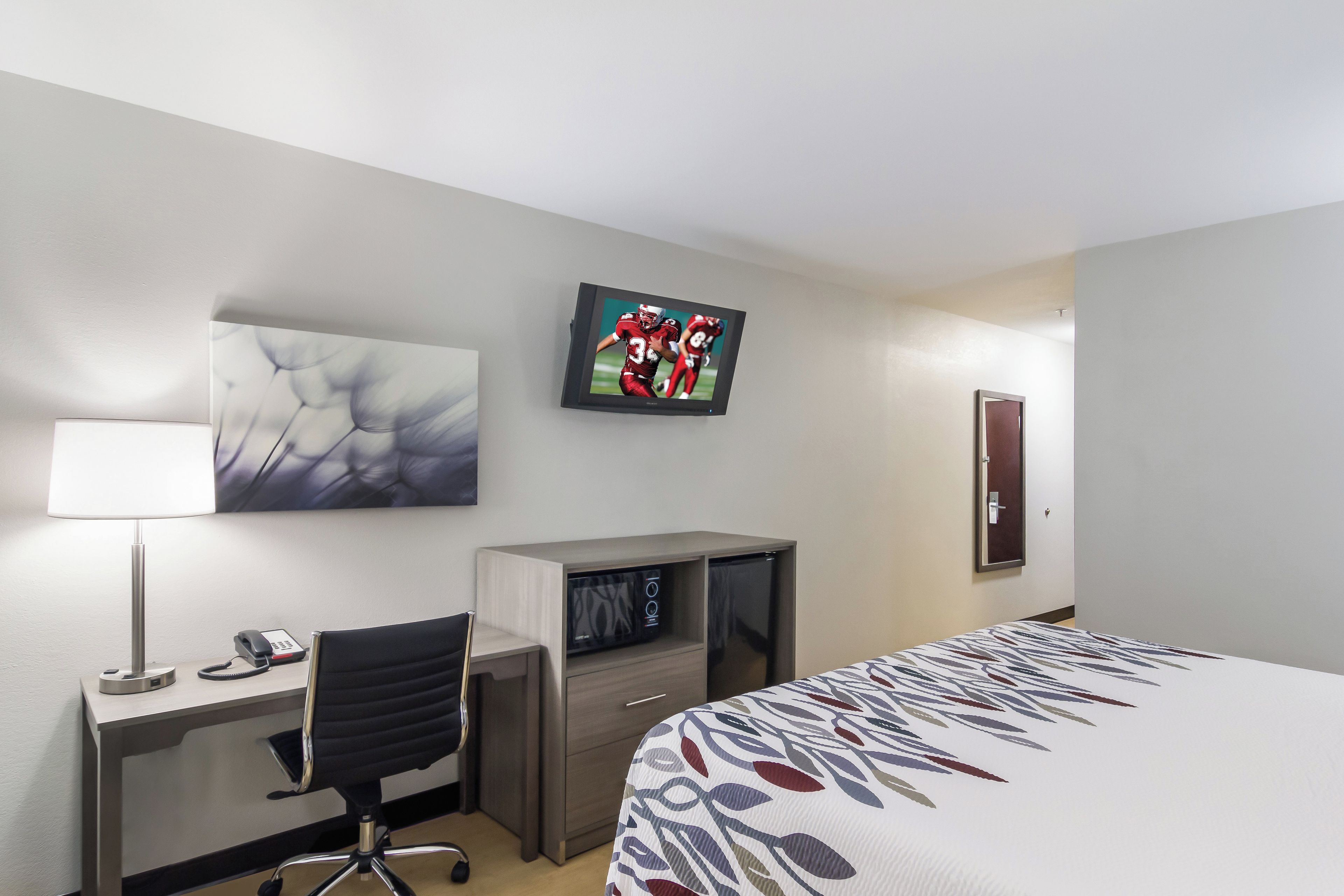 A hotel room with a bed, a desk with a chair, a television, a telephone, and a wardrobe.