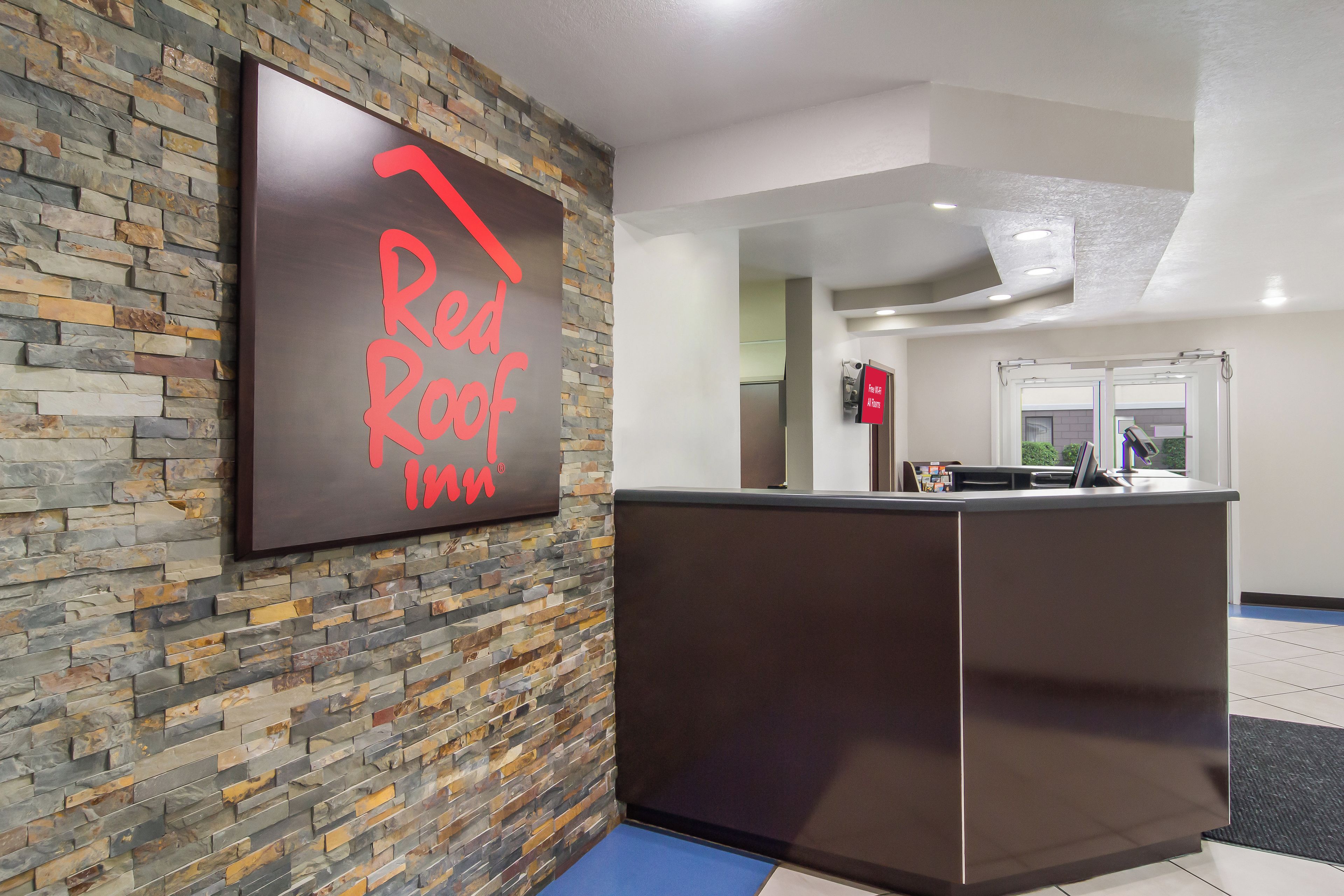 A reception desk with a stone wall backdrop and a sign that reads 'Red Roof Inn'.