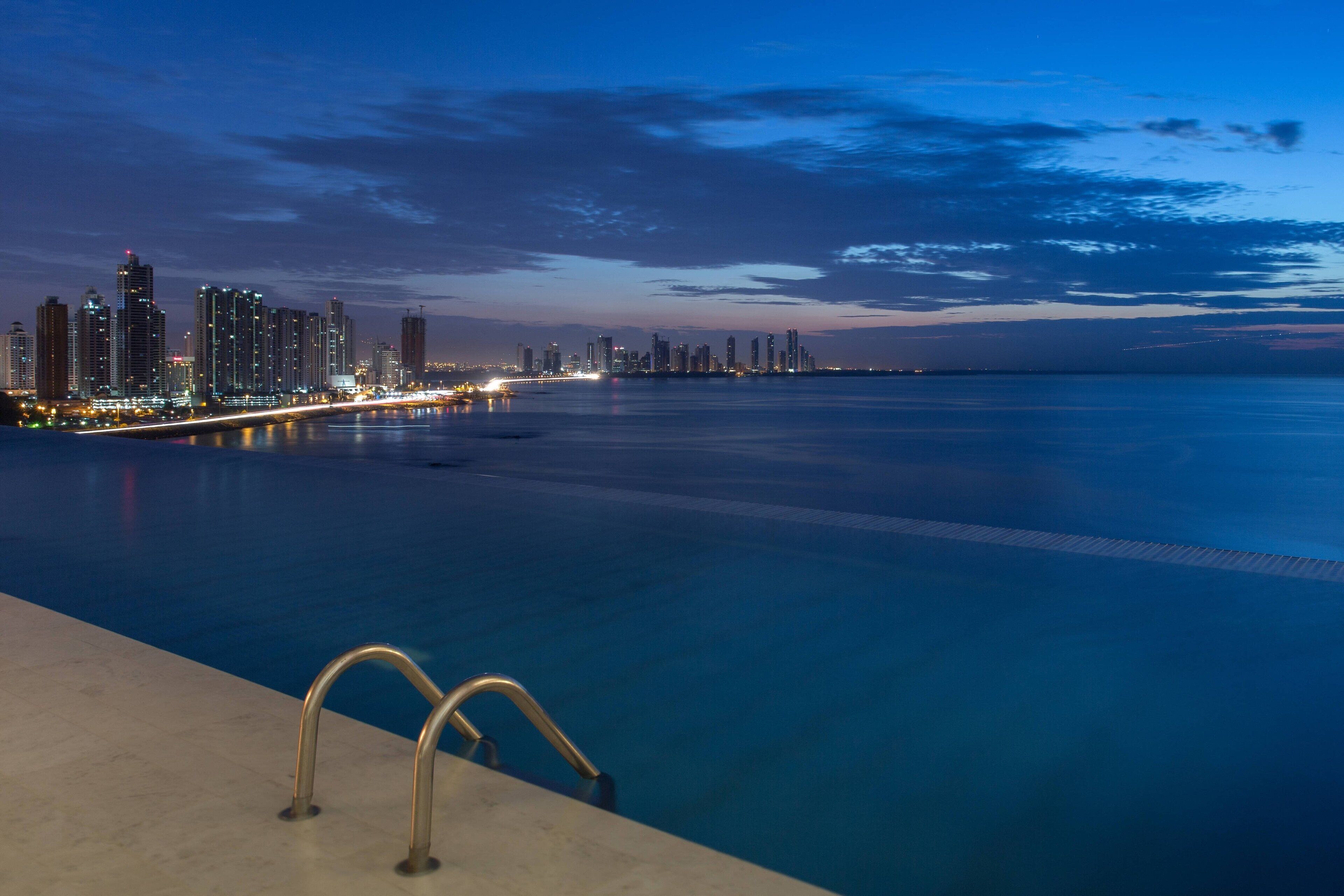 Una piscina amb vistes al passeig marítim i un skyline urbà al fons.