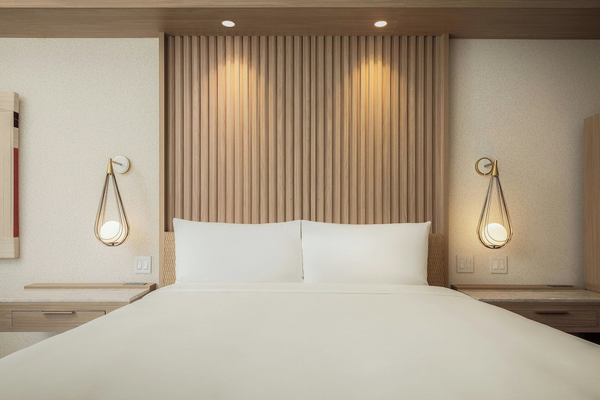 Habitación de hotel moderna con una cama grande, cabecero de madera y lámparas colgantes.