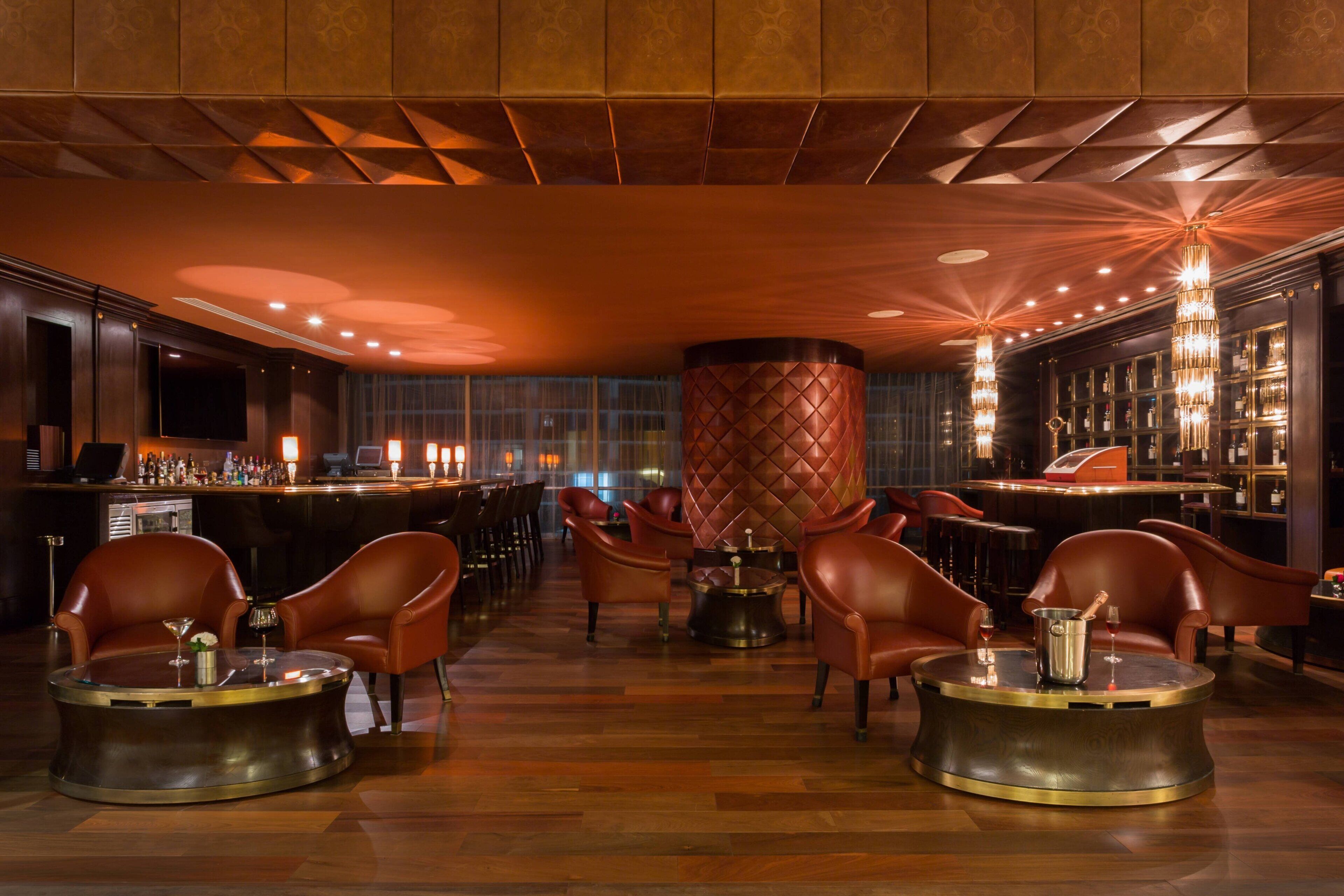 A bar area with leather chairs, a round table, and a bar counter with bottles.