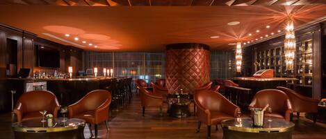 A bar area with leather chairs, a round table, and a bar counter with bottles.