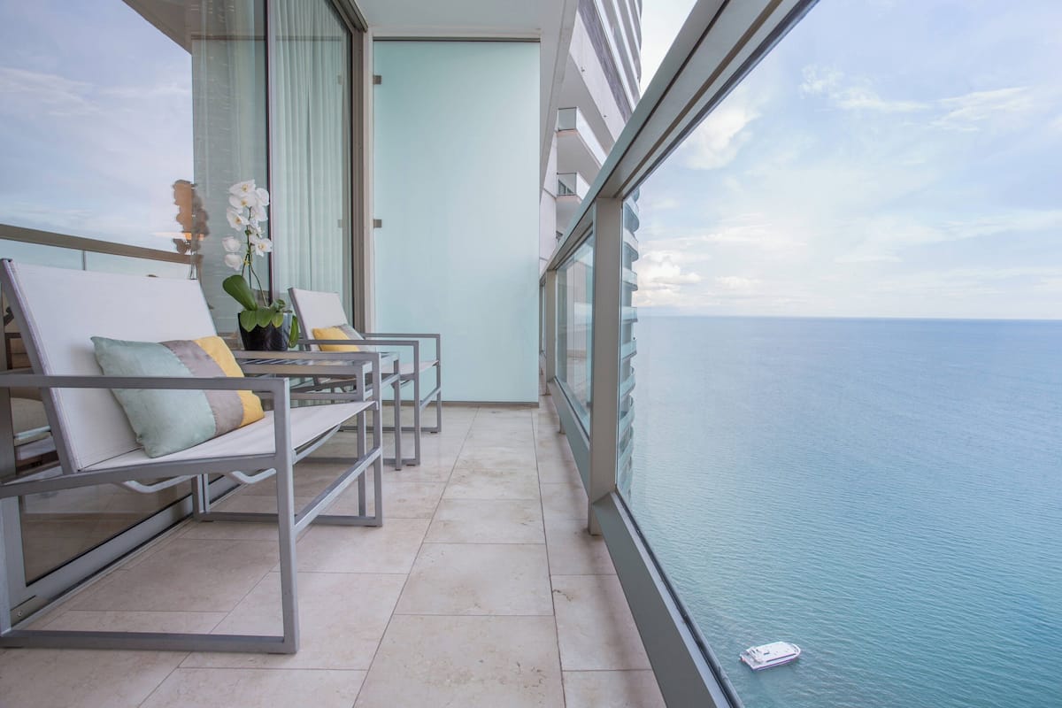 Un balcón con dos sillones, una orquídea en maceta y vista al mar.