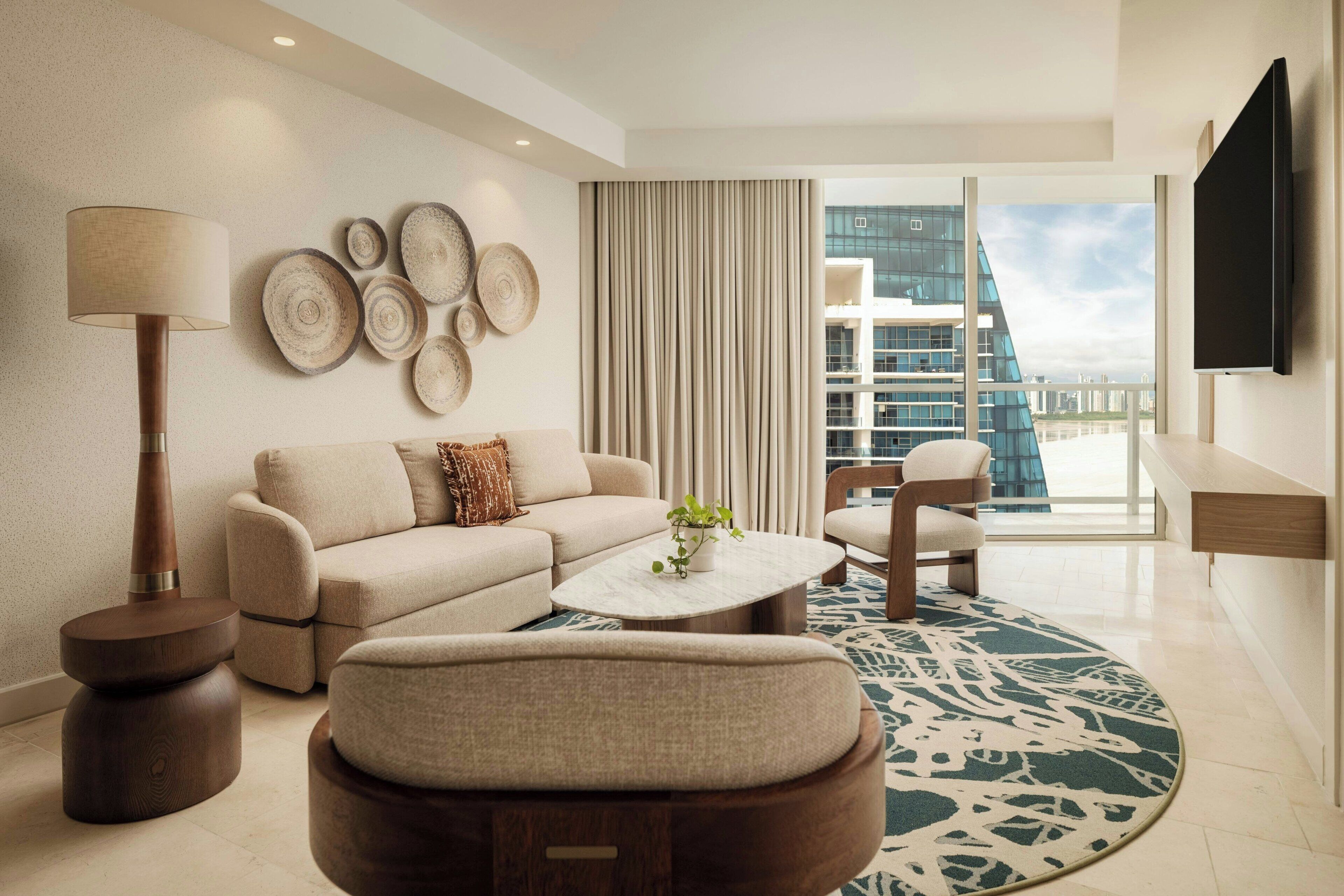 A modern living room with a sofa, armchair, coffee table, and a large window with a city view.