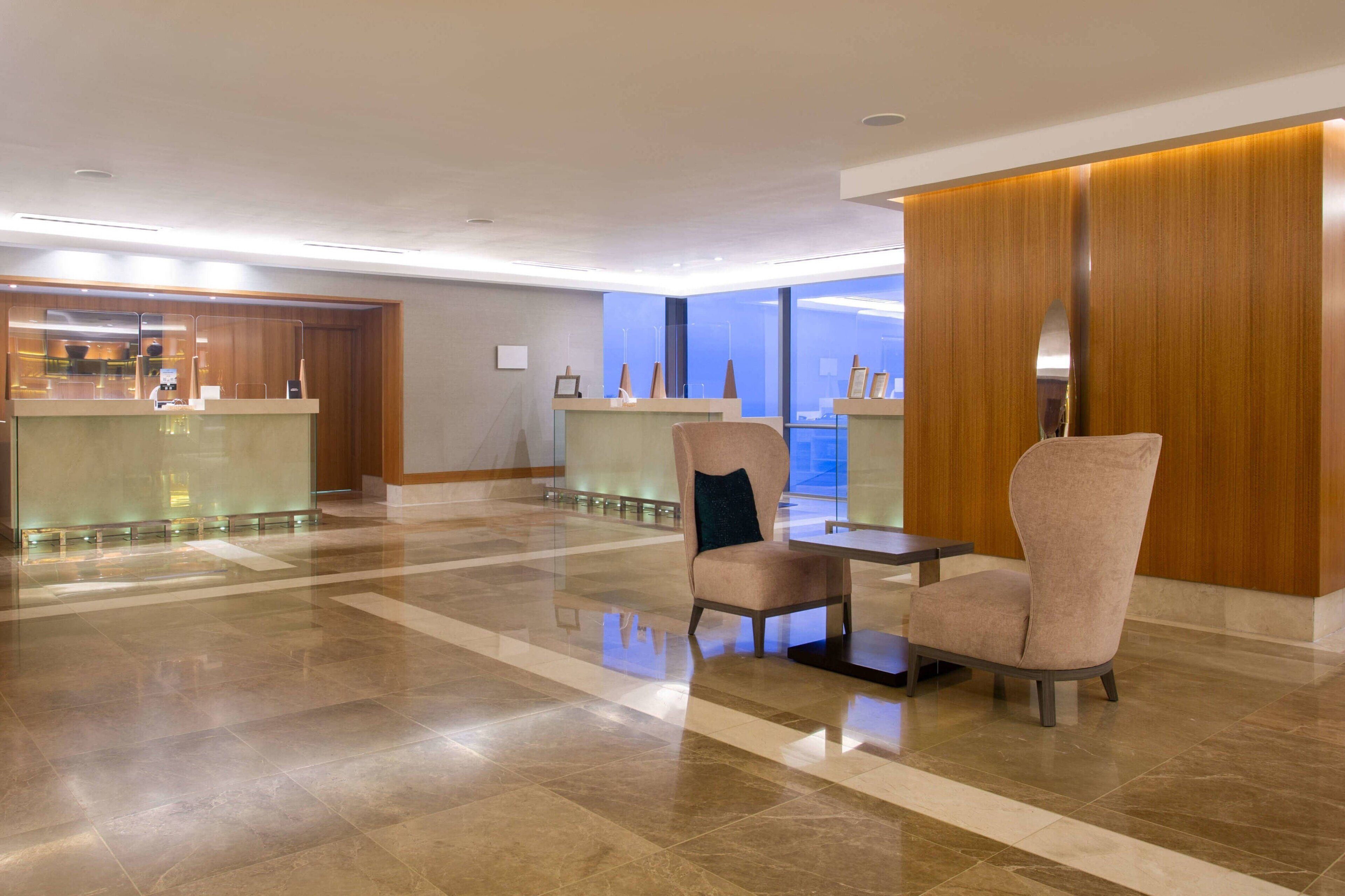 A modern lobby with a reception desk, seating area, and large windows.