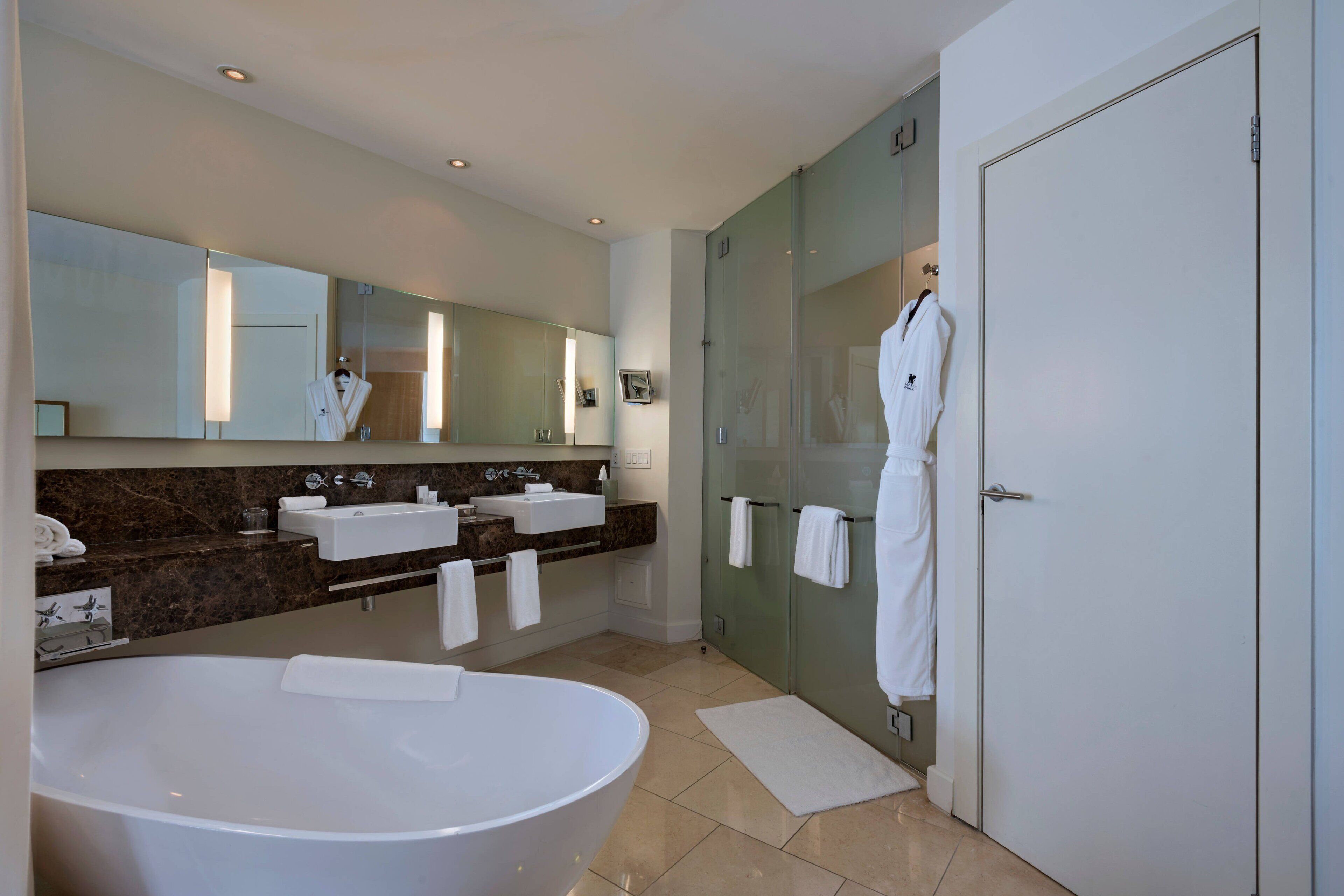 Une salle de bain moderne dotée d’une grande baignoire sur pieds, de deux vasques, d’une douche à parois de verre et d’un grand miroir sur toute la hauteur du mur.