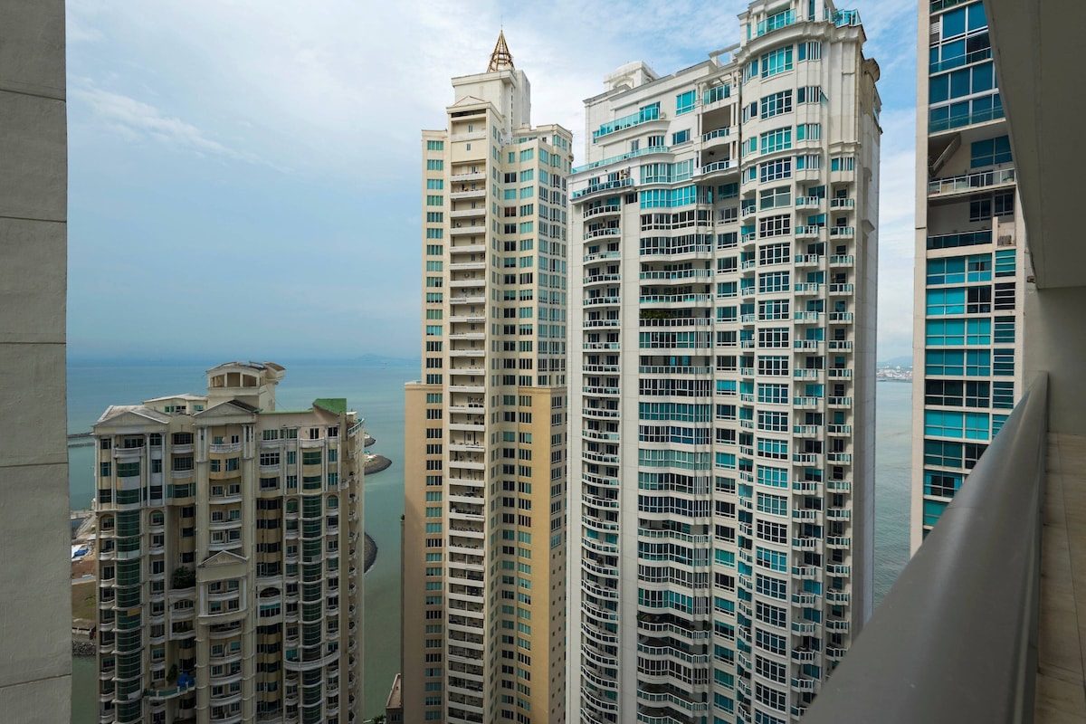 High-rise buildings with balconies, a clear sky, and a body of water in the background.