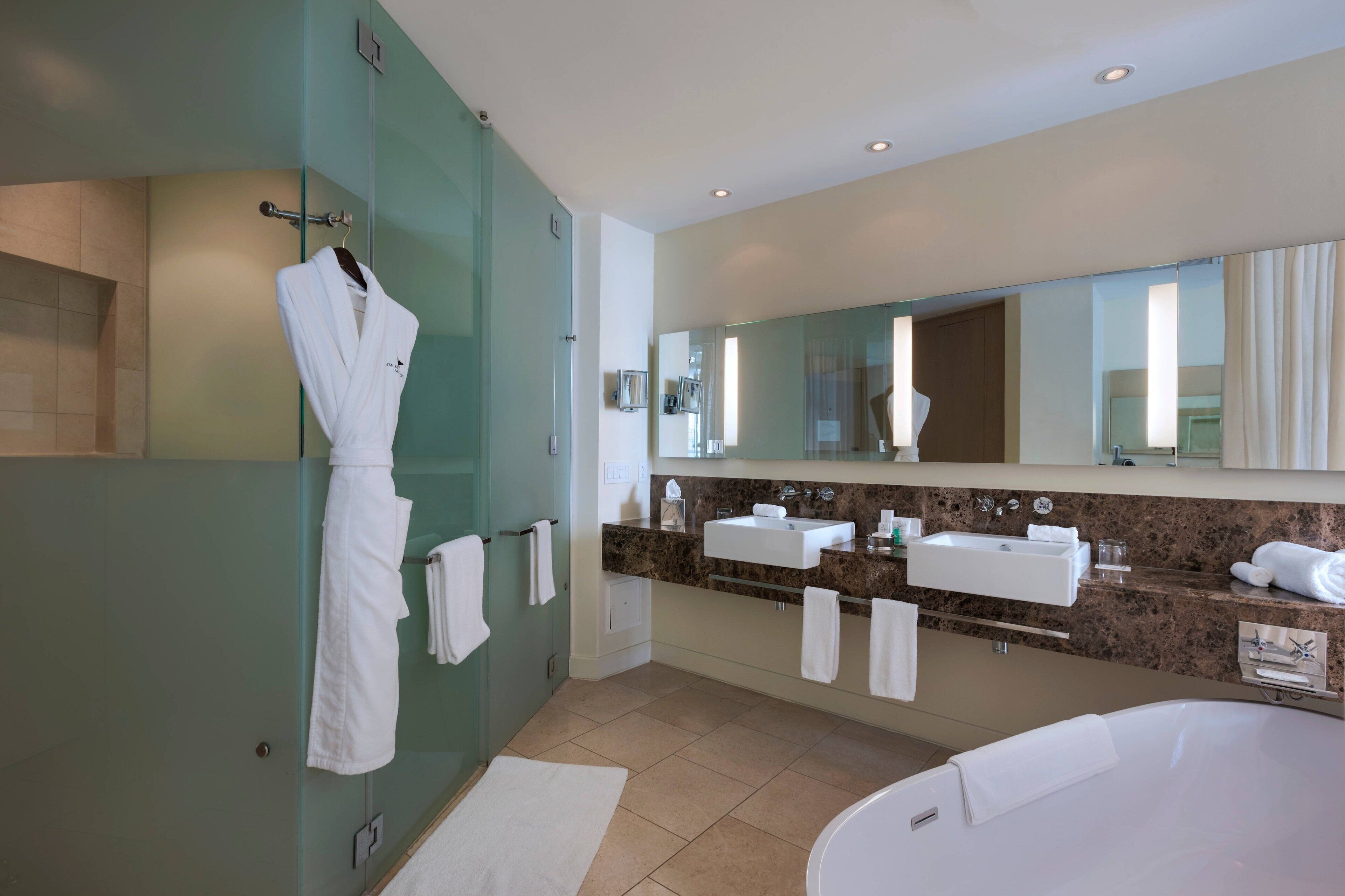 Ein modernes Badezimmer mit Duschkabine aus Glas, großem Spiegel, zwei Waschbecken und einer Badewanne.