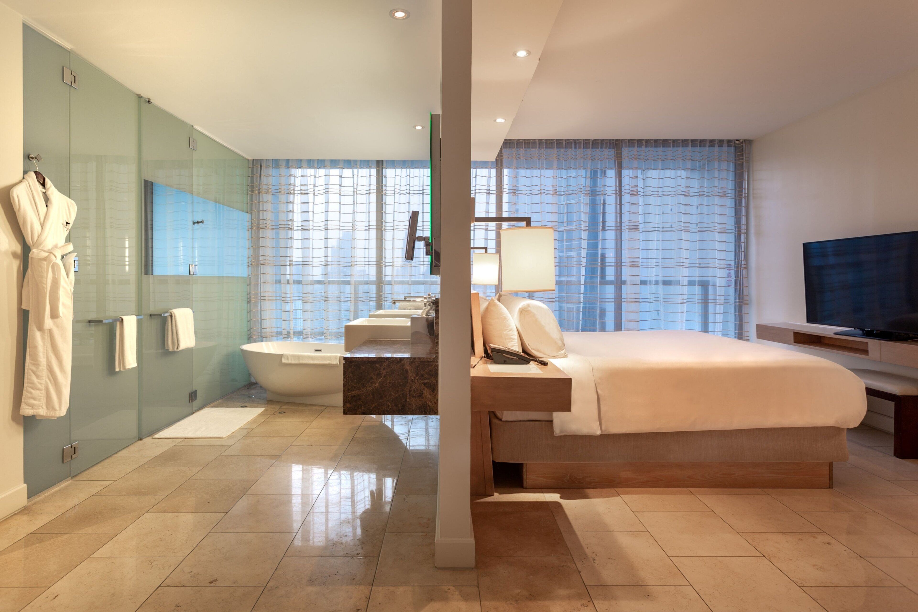Une chambre d’hôtel moderne dotée d’un grand lit, d’une baignoire et d’une douche séparée par des parois en verre.