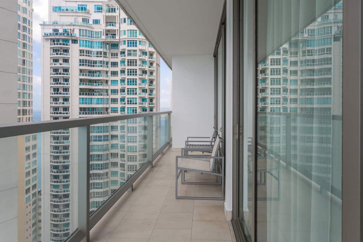 Un balcón con barandilla de vidrio, un banco de metal y vistas a rascacielos.