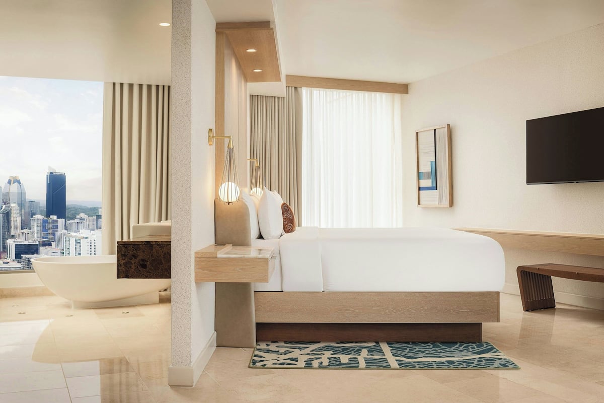 Una habitación de hotel moderna con una cama grande, una bañera, vistas a la ciudad y un televisor de pantalla plana.