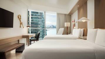 Habitación de hotel con dos camas, un escritorio, una silla, un televisor y vistas a un horizonte urbano.