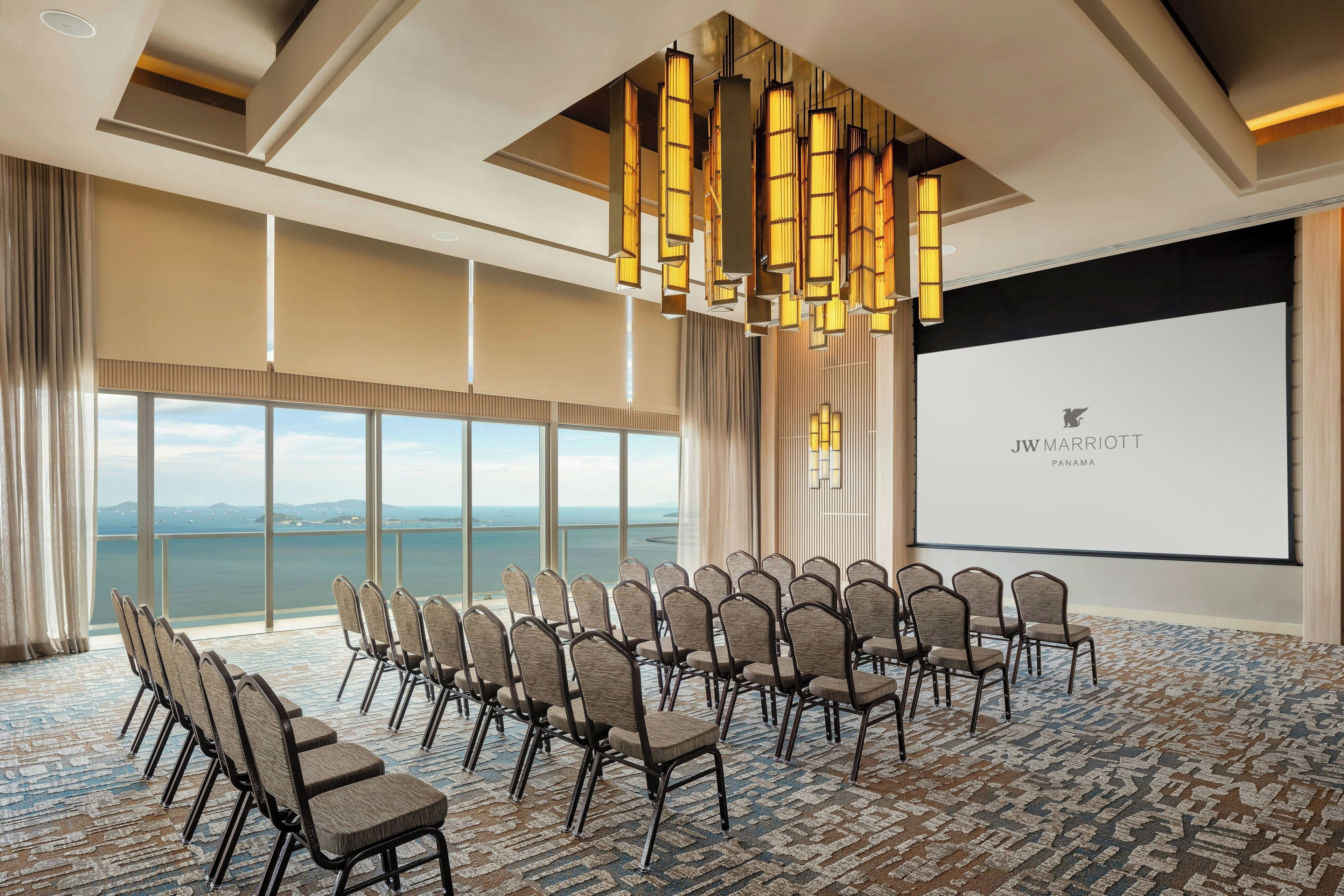 A conference room with a large screen, rows of chairs, and a view of the sea.